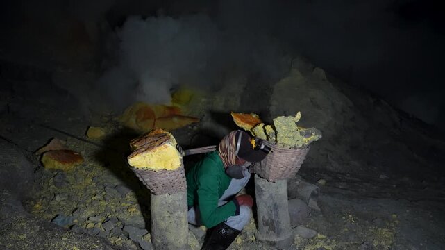 Kawah Ijen miner wearing respirator picks up sulfur chunks loaded in baskets