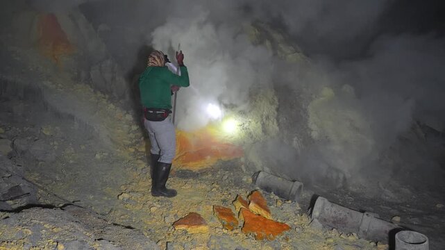 Inside Kawah Ijen volcano in East Java, Indonesia, a sulfur miner uses a crowbar to break sulfur deposits amid dense fumes and harsh crater conditions at night