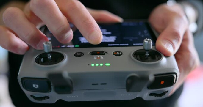 Close up of a pilot's hands operating a modern drone remote control. The person is using the sticks and buttons to fly the quadcopter