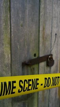 Yellow police tape with the words crime scene do not enter cordoning off an area in front of an old wooden door. Which is secured by a rusty padlock. Suggesting an investigation or prohibited area