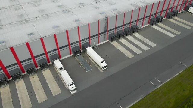 High angle view of a large logistics hub with multiple semi trucks parked at the loading docks for unloading and distributing cargo, showcasing the modern industrial supply chain process