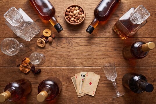 Whisky bottles, decanters, glasses, nuts and playing cards on wood