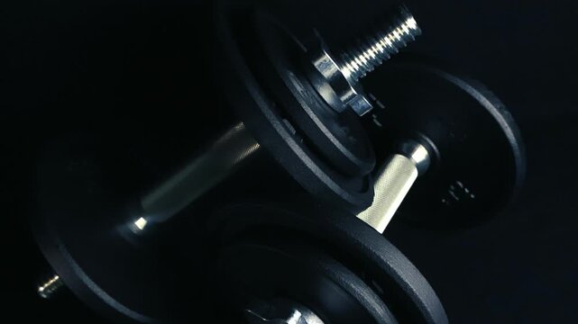 Steel dumbbell with changeable weight discs sitting on a dark background, representing gym equipment for bodybuilding, fitness workouts, and intense physical exercise in a professional gym setting