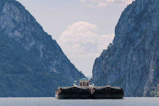 Cargo barge sailing on water between high mountains and steep cliffs of Iron Gates Gorge, demonstrating Danube river transport in a natural landscape