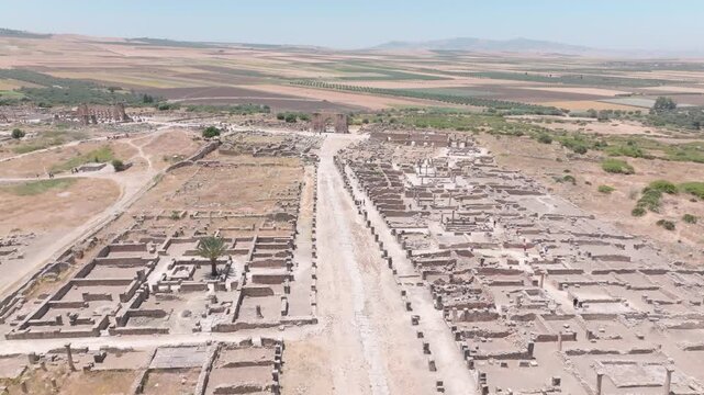 High aerial view of the archaeological site of Volubilis in Morocco, revealing an extensive ancient street network, building foundations, excavated ruins and the surrounding agricultural landscape.