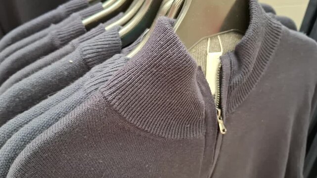 Dark blue knitted sweaters with high collars and zippers hanging on clothes hangers in a store shop, fashion apparel, retail display, casual wardrobe.