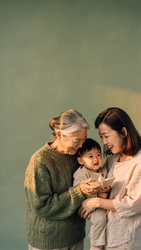Multi-generational Asian family with grandmother mother and toddler holding a paper boat in warm sunlight