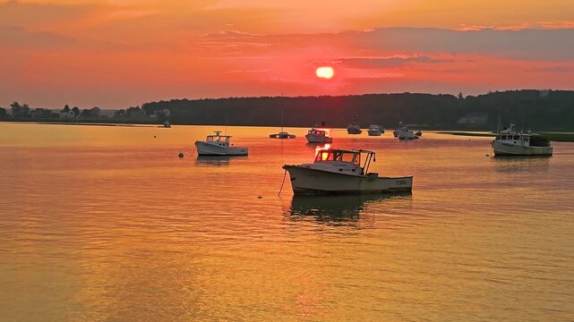 Beautiful coastal harbor at sunset with fishing boats, glowing sun path on water, warm summer sky, and peaceful seaside atmosphere for travel or nature videos.