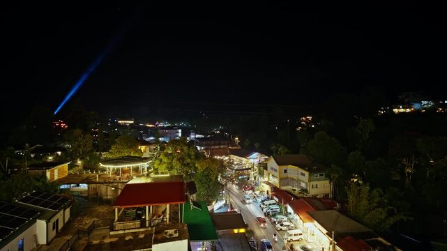 A blue searchlight beam cuts across the night sky above Ella while the lights of hotels, shops and parked cars glow in the dark valley below.