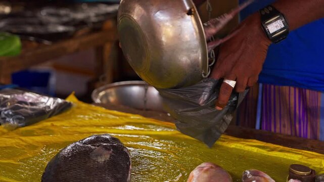Fresh fish are weighed in the pan of an old hanging scale as a vendor holds open a plastic bag over the vivid yellow counter of a coastal fish market in Sri Lanka, a fast and practised exchange.