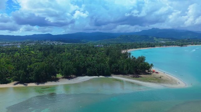 Expansive high-altitude aerial perspective showing the entire coastline of Luquillo Beach with the lush green mountains of El Yunque National Forest in the background.