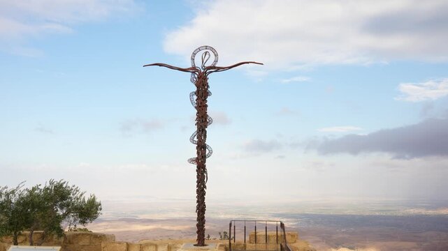 Bronze Serpent Cross sculpture stands on Mount Nebo above the Jordan Valley, captured in a smooth left pan.