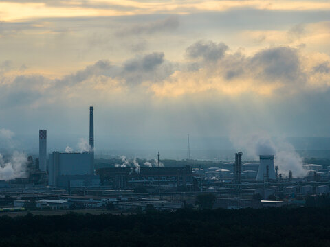 Schwedt Oder, Germany - 20 August 2026: Aerial view of PCK Raffinerie GmbH with industrial chimneys, cooling towers, and steam plumes under a cloudy sky at sunset.