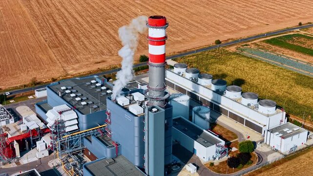 Flying around the plant with a tall smokestack. Vast agricultural fields are around the industrial facility.