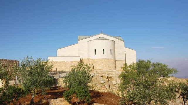 Handheld panning view, Memorial Church of Moses on Mount Nebo near Madaba, Jordan, seen among olive trees under a clear blue sky at the historic Christian pilgrimage site
