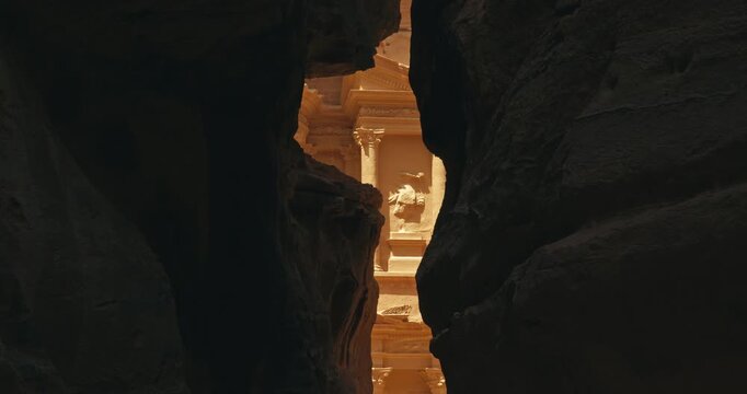 View through the narrow sandstone walls of the Siq revealing Al Khazneh Treasury in Petra, Jordan illuminated by warm natural daylight.
