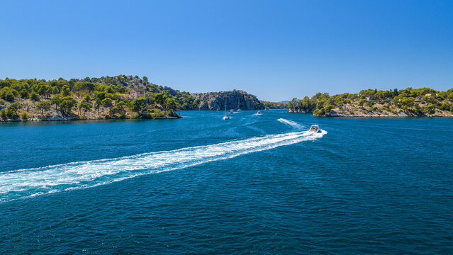 Aerial view of Luka Channel near &Scaron;ibenik, Croatia, with a speedboat crossing the blue Adriatic waters, leaving a long white wake between rugged pine-covered islands under a clear sky.