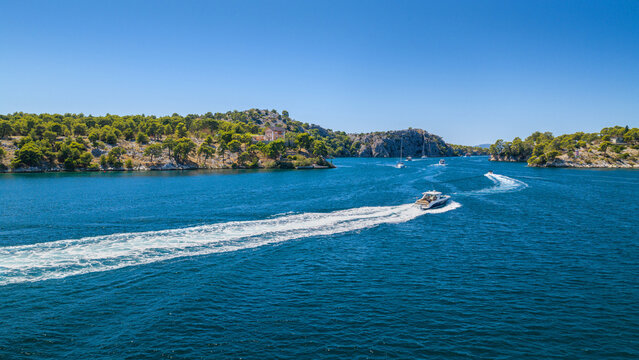 Aerial view of Luka Channel near &Scaron;ibenik, Croatia, with a speedboat crossing the blue Adriatic waters, leaving a long white wake between rugged pine-covered islands under a clear sky.