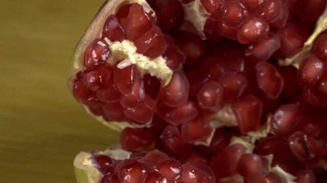 Close up panning shot of fresh pomegranate seeds inside cut fruit. Glossy red arils and pale membranes fill the frame, showing detailed texture and natural variation