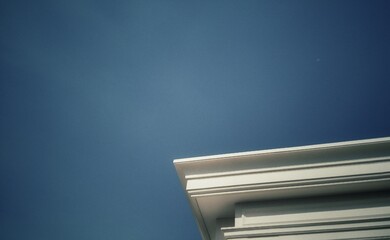 Minimalist white architecture cornice corner against a clear blue sky. Artistic low angle shot with vintage analog film style photography, subtle grain texture, and nostalgic mood. © muhtadi