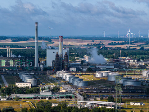 Schwedt Oder, Germany - 20 August 2026: Aerial view of PCK Raffinerie GmbH featuring large storage tanks, industrial chimneys, and processing units under a cloudy sky.