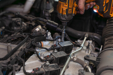 Fototapeta premium Mechanic hand holds cordless driver over exposed engine parts. Bolt fastening happens among cables, clamps, and silver housings during automotive service and engine maintenance work.