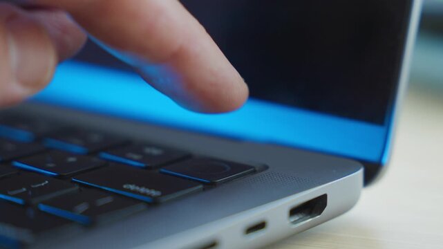 Close up on finger touching a laptop computer fingerprint recognition pad. Unlocking device with user fingerprint or changing system without password person clicks keyboard key in dark office desk
