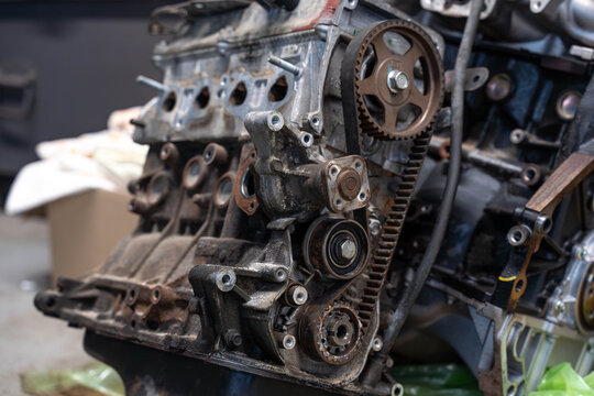 Close mechanical detail of engine housing shows timing belt, gear wheel, and pulleys with worn cast metal. Grease, corrosion, and bolt holes give strong industrial texture for repair themes.