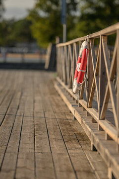 Red and white lifebuoy hanging on wooden marina railing.