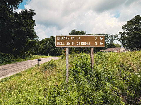 Brown metal directional sign pointing toward popular hiking trails and waterfall destinations in Southern Illinois' Shawnee National Forest.