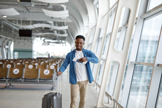 A young man happily walks through a bright, contemporary airport terminal with his luggage and travel documents in hand