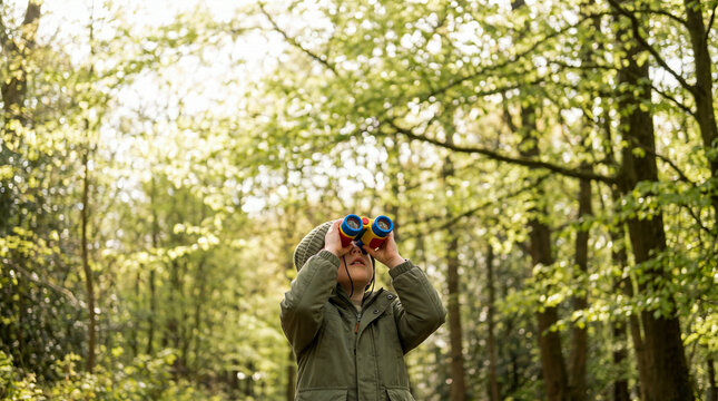 Curious young boy exploring nature and looking up through binoculars in a lush green forest
