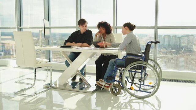 Teamwork brainstorm. Diverse multiracial colleagues woman in chair for people with disability working together. Group of people sitting in creative office discussing business. Young professional team