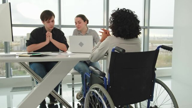 Teamwork brainstorm. Diverse multiracial colleagues woman in chair for people with disability working together. Group of people sitting in creative office discussing business. Young professional team