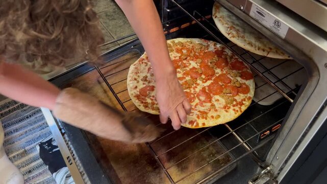 Person wearing oven mitt pulling hot pizza out of oven