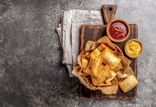 Fried cheese empanadas. Traditional Latin American snack served on wooden board with chili sauce and mustard. Top view, stone background