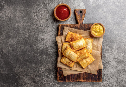Fried cheese empanadas. Traditional Latin American snack served on wooden board with chili sauce and mustard. Top view, stone background