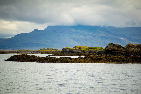 Seaweed covered basalt rocks in coastal bay with view of Hafnarfjall mountain range under low clouds in Akranes Iceland