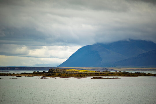 Basalt rock island in bay with majestic mountain peak shrouded in clouds in Akranes Iceland
