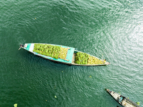 Rangamati Hill District, Chittagong Division, Bangladesh - 30 September 2023: Aerial view of a wooden boat heavily loaded with green produce navigating the calm waters of Kaptai Lake.