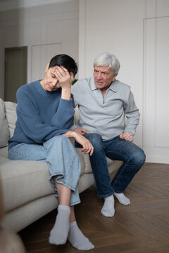 Exhausted unhappy senior woman sitting on sofa tired of angry conversation with elderly husband, depressed sad wife on couch distancing from irritated narcissistic constantly displeased partner.