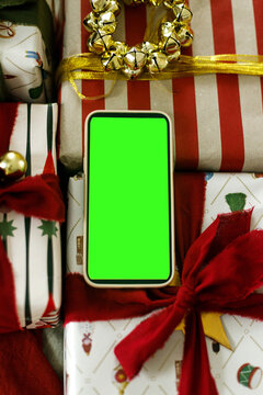 Smartphone green screen mockup lying on gift boxes top view, concept of Christmas online shopping, holiday discount, seasonal app, ecommerce and mobile marketing