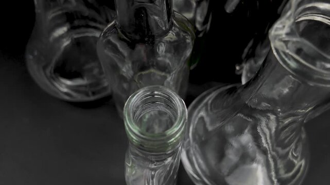 Small transparent glass bottles of various shapes stand on a black background, versatile containers used for storage of different objects and liquid. Glass bottles collection, top view