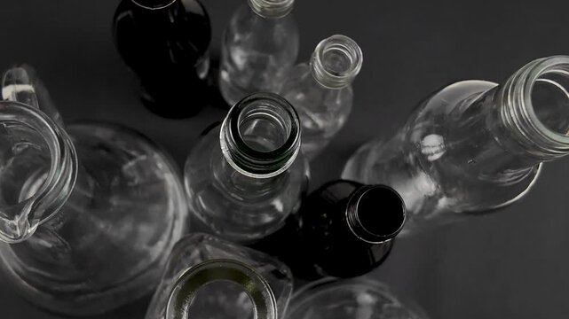 Small transparent glass bottles of various shapes stand on a black background, versatile containers used for storage of different objects and liquid. Glass bottles collection, top view
