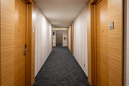 Long modern hotel corridor with wooden doors dark carpet and elevator at the end