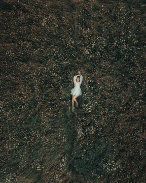 Czech Republic - 18 June 2025: Aerial view of a woman in a white dress lying in a field of wildflowers.