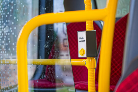 Yellow stop request button on public bus with red seats and rainy window