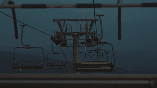 View of empty ski chairlift chairs swaying gently in the wind against a dark atmospheric sky at Babin Zub resort on Stara Planina, Serbia. Off season mountain resort mood footage.