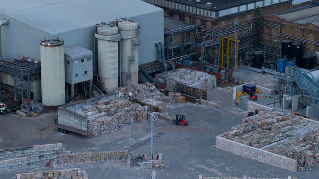 Sittingbourne, United Kingdom - 30 July 2026: Aerial view of DS Smith Kemsley Paper Mill with stacks of recycled paper bales, industrial silos, and forklifts in the yard.