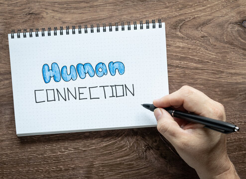 Human Connection handwritten on white spiral notebook flat lay background with real hand holding a black ink pin.